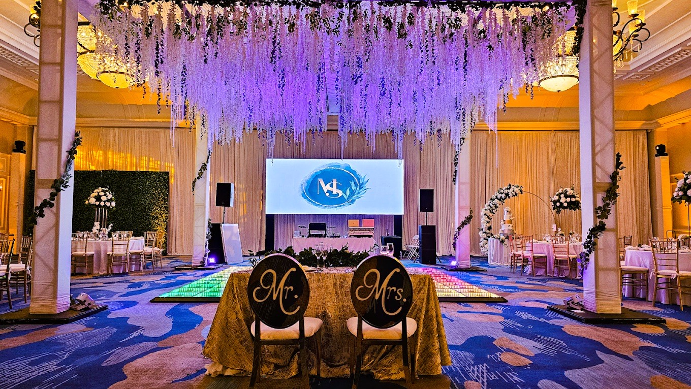 Ballroom wedding reception produced by Sound Level Events, with a draped floral ceiling installation, uplighting and a projection screen